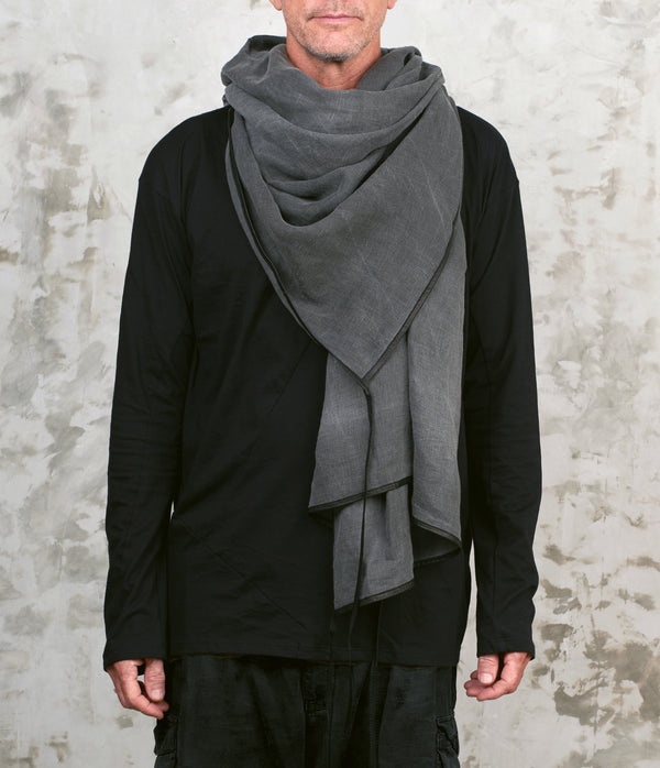 Person wearing a gray linen scarf over a black outfit against a textured wall.